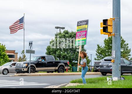 Sterling, USA - September 12, 2020: Candid woman holding Ashley homestore store sign advertisement by store strip mall road sidewalk in Loudoun county Stock Photo