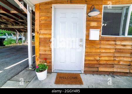 White front door decorated with flowers on a pot and doormat with welcome sign Stock Photo