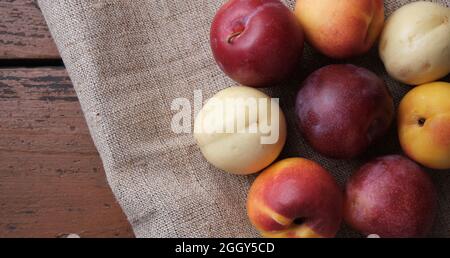 Juicy fruits in a linen tablecloth on a old wooden table. Plums, apricots on a dark red background. Top view. Stock Photo