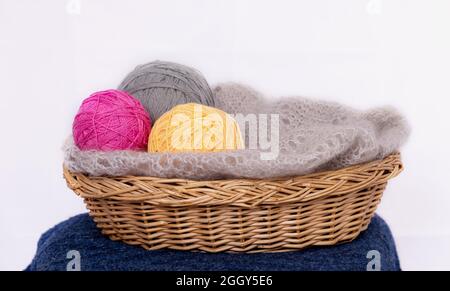 Pink, gray and yellow thread balls for knitting in a basket and gray scarf on a light background. Knitting Stock Photo