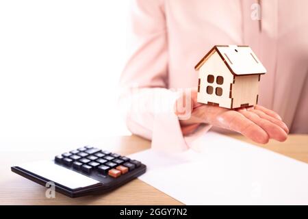 Woman holds model of house on hand, on the table lies a contract and calculator Stock Photo