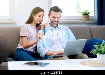 Happy couple couple e-shopping on internet. Woman using credit card, man with laptop Stock Photo