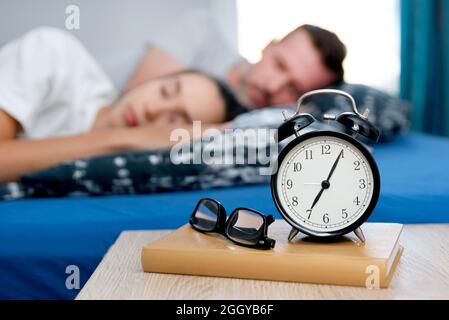 Couple sleeping in bed. Alarm clock on the nightstand. Healthy sleep concept Stock Photo