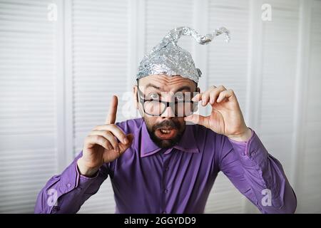 Bearded funny man in cap of aluminum foil. Concept art phobias. Conspiracy theory. Conspiracy. Insanity. Stock Photo