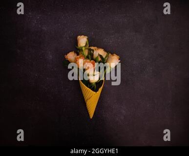 A beautiful bouquet of orange roses emerging from a bright yellow cone on a dark marbled background. Dreamy romantic summer present concept. Stock Photo