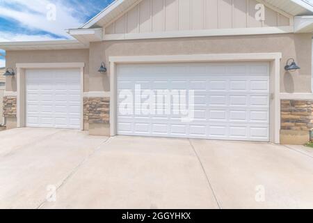 Exterior of a garage with white double sectional doors and wall mounted lighting fixtures Stock Photo