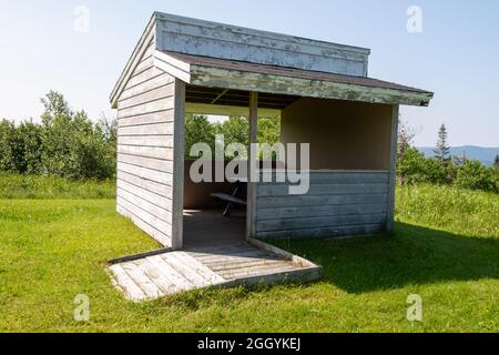 A wooden camp cookhouse with a picnic table inside the building at a campground. The wood board structure is in the middle of a green grass garden. Stock Photo