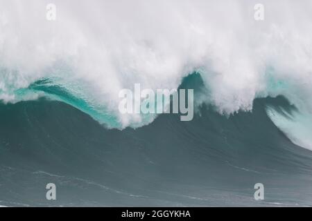 An angry turquoise green color massive rip curl of a wave as it barrels rolls along the ocean. The white mist and froth from the wave are foamy. Stock Photo