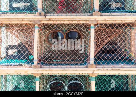 Multiple rope netting lobster pots or traps stacked high along a wharf. Containers are made from an orange wire, nylon netting, and in a square shape. Stock Photo