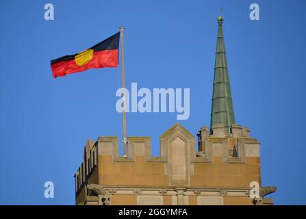 Red, yellow and black aboriginal first nations flag flying atop a sandstone building against a blue sky backdrop