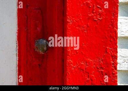 A closeup of an antique rusty iron decorative metal door handle on a brightly painted vibrant red wooden door. Stock Photo