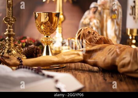 Catholic symbols composition. Religion concept. Jesus figure,The Cross, monstrance,  Holy Bible, rosary and golden chalice on the wooden altar. Stock Photo