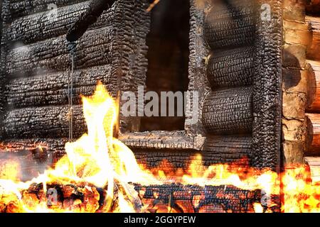 Wooden house after the fire. Coals on the logs. The ashes of the house from fire. Burnt destroyed cottage. Stock Photo