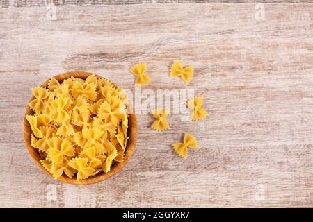 Farfalle pasta in wooden bowl on wooden backgraund. Uncooked dried durum wheat semolina pasta. Italian noodles. Stock Photo