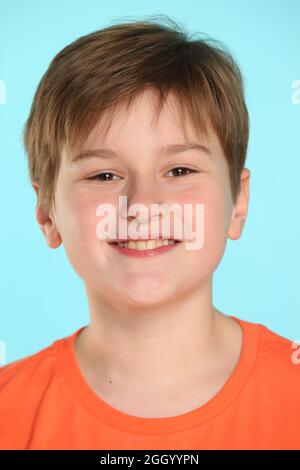 Close-up portrait: a handsome developed cheerful teenage boy in an orange T-shirt smiles and looks eye to eye. Stock Photo