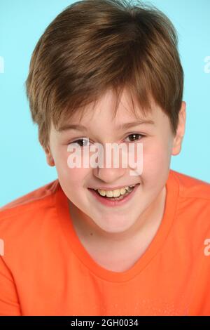 Close-up portrait: a handsome developed cheerful teenage boy in an orange T-shirt laughs to tears and looks eye to eye. Stock Photo