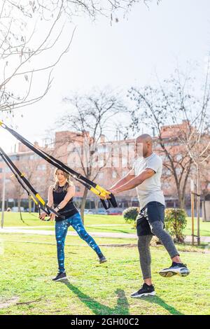 Fitness couple doing legs exercise with fitness straps in park Stock Photo