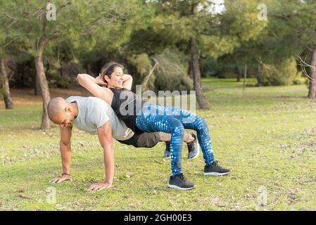 Fitness couple doing back to back lifting exercise in the park Stock Photo