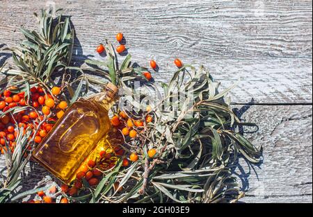 A jar with sea buckthorn oil and a fresh branch of sea buckthorn with berries on a wooden background. Sea buckthorn oil, antioxidant and vitamins Stock Photo