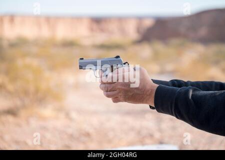 Hand of a man holding a small silver gun aiming on the left Stock Photo