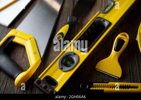 Contractor concept. Tools of the contractor: yellow hardhat, libella, hand saw, and notebook on the rustic wooden table. Stock Photo