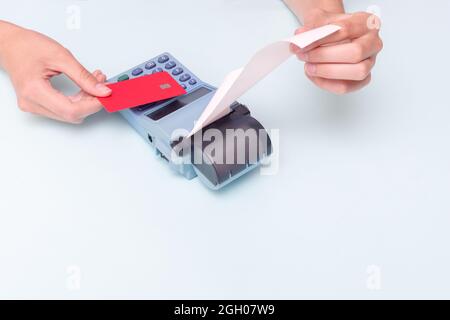 Payment for purchases by credit card. Close-up of a hand holding a bank card and a hand holding a check, receipt on a cash register on a blue backgrou Stock Photo