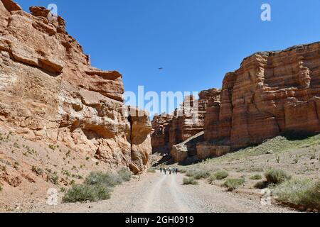 Tourists travel along the bottom of a deep warn colored canyon accompanied by a drone, blue sky Stock Photo