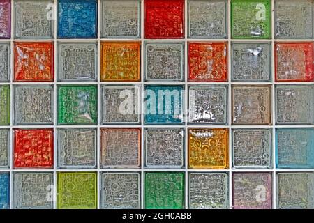 A colorful stained glass window. Rows of glass squares in blue, red, yellow and greenish shades with a textured surface and highlights Stock Photo