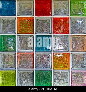 A colorful stained glass window. Rows of glass squares in blue, red, yellow and greenish shades with a textured surface and highlights Stock Photo
