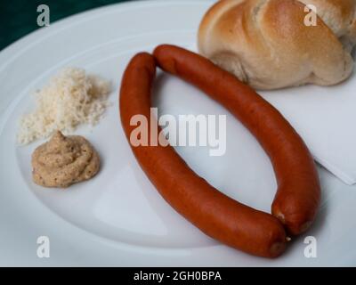 Debrecener Sausage with Mustard, Horseradish and Kaiser Roll Served on a White Plate Side View Stock Photo