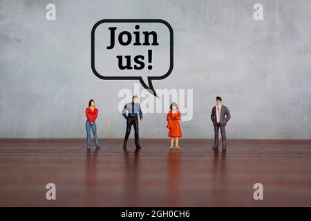 Miniature people on table against concrete wall with text JOIN US! Stock Photo