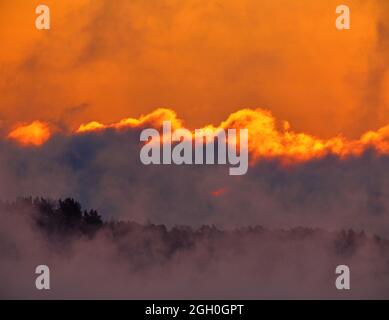 Dramatic scene including fiery sunrise on extremely cold winter morning with sea fog and icy covering Baltic sea and clouds appearing as if in flame o Stock Photo