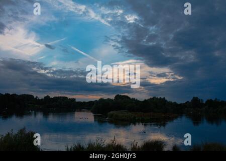 Blue sky and clouds at sunset over trees and a lake at Lackford Lake in Suffolk Stock Photo