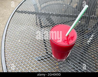 A clear glass with red smoothie beetroot based fruit drink viewed from above with straw.Sat on a contrasting black lattice work Stock Photo