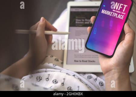 Business with NFT crypto art on mobile phone. Woman using smartphone with non fungible token logo on the screen. Concept of future workspace  Stock Photo