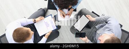Business people sit on chairs with tablet and commercial business charts and discuss work plans top view Stock Photo