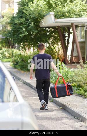 Messenger in black uniform with thermo bag runs on foot really fast to deliver quickly hot pizzas just baked Stock Photo