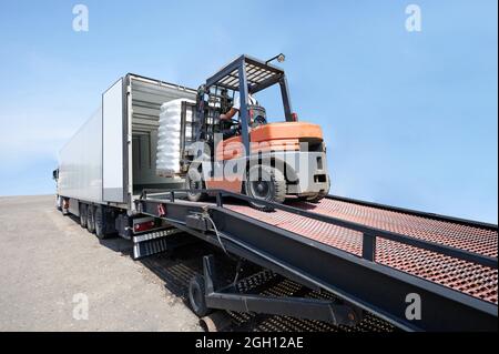 Forklift load pallet with cargo to truck isolated on blue sky background Stock Photo