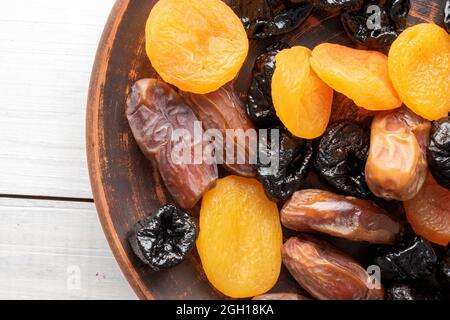 Several appetizing dates, dried apricots, prunes in a clay plate on a wooden table, close-up, top view. Stock Photo