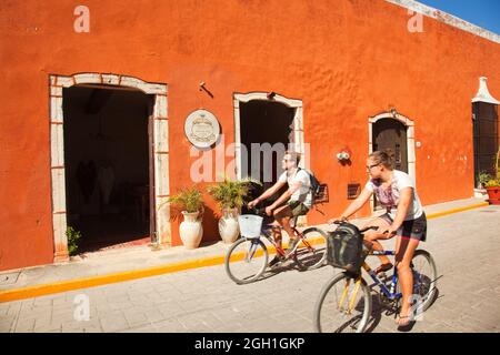 Tourist couple riding on bikes in front of the colorful colonial buildings at the historic center, Valladolid, Yucatan Province, Mexico, Central