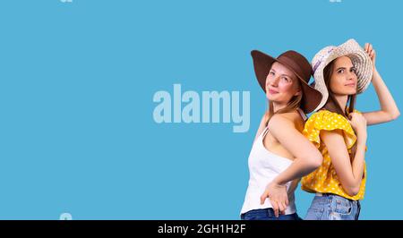 Two amazing young women wearing the hats standing back to back each other and looking up with smiling face. Stock Photo