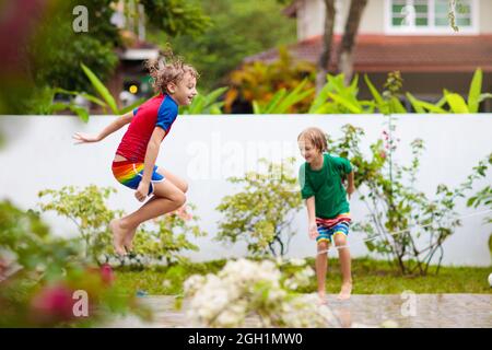 Kids playing with water hose in summer garden. Child water sprinkler fun on hot sunny day. Children jump and run in the backyard. Stock Photo