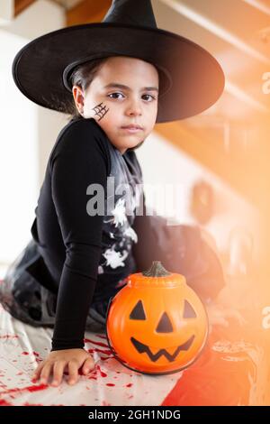 Portrait of caucasian little girl in witch costume next to a pumpkin. Halloween party. Stock Photo