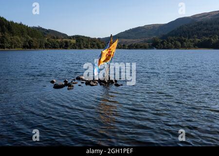 Loch Lubnaig, Callander, Loch lomond and Trossachs National Park, Scotland. 2 September 2021. PICTURED: The Saltire & Lion Rampant (Royal Banner) flags poke out of the water in the middle of Loch Lubnaig. Loch Lubnaig (Loch Lùbnaig in Gaelic) is a small freshwater loch near Callander in the Stirling council area, Scottish Highlands.  The loch nestles in the space between Ben Ledi and Ben Vorlich. Fed by the River Balvaig from the north and drained by the Garbh Uisge to the south, Loch Lubnaig offers fishing from the shore while canoes can be rented at the north end. Alternatively, two car park Stock Photo
