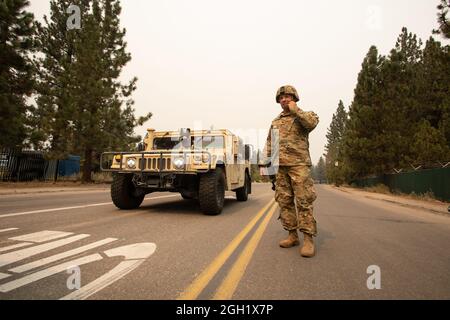 U.S. Army Spc. Dace Taylor, from the California Army National Guard’s 270th Military Police Company, adjusts the chin strap of his helmet while talking to another Soldier, Sept. 1, 2021, in South Lake Tahoe, California, as the Caldor Fire encroaches on the evacuated city. Cal Guard activated 150 military police Aug. 30 to support the California Highway Patrol with checkpoints at hard closures while the area is evacuated. (U.S. Air National Guard photo by Staff Sgt. Crystal Housman) Stock Photo