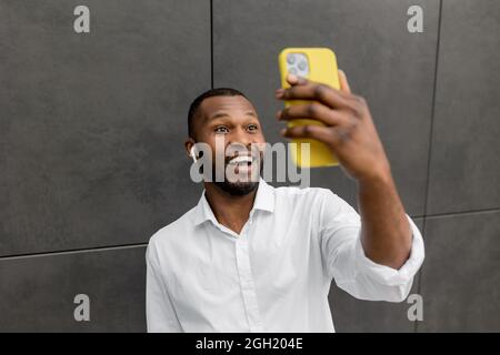 Joyful african american businessman holding smartphone, having an online video call with colleague. Stylish male employee or student received great Stock Photo