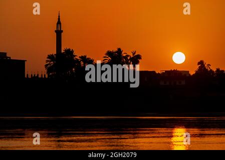 View across large wide river Nile in Egypt through rural countryside landscape with beautiful orange sunset and mosque minaret architecture Stock Photo