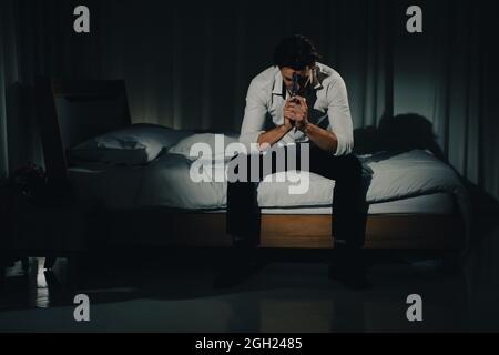 A young man in casual business clothes sitting alone in bedroom holding a pistol in a thoughtful and serious mind look like going to kill himself. Con Stock Photo