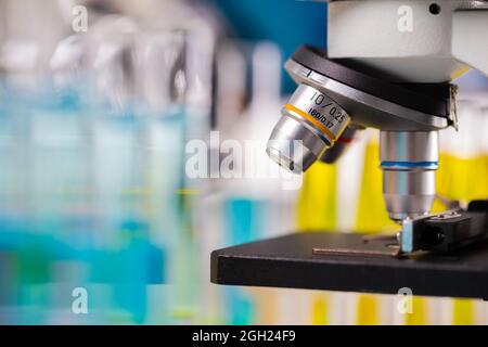 Close up focus of microscope lens with blur colorful background of test tubes and beakers copy space. Stock Photo