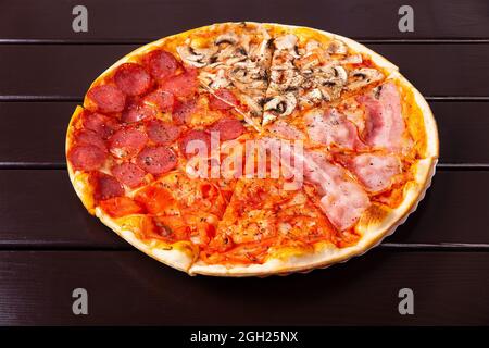 Fresh Italian Four Seasons Pizza or Pizza Quattro Stagioni on the wooden kitchen table with different bright ingredients. Focus stacking. Stock Photo